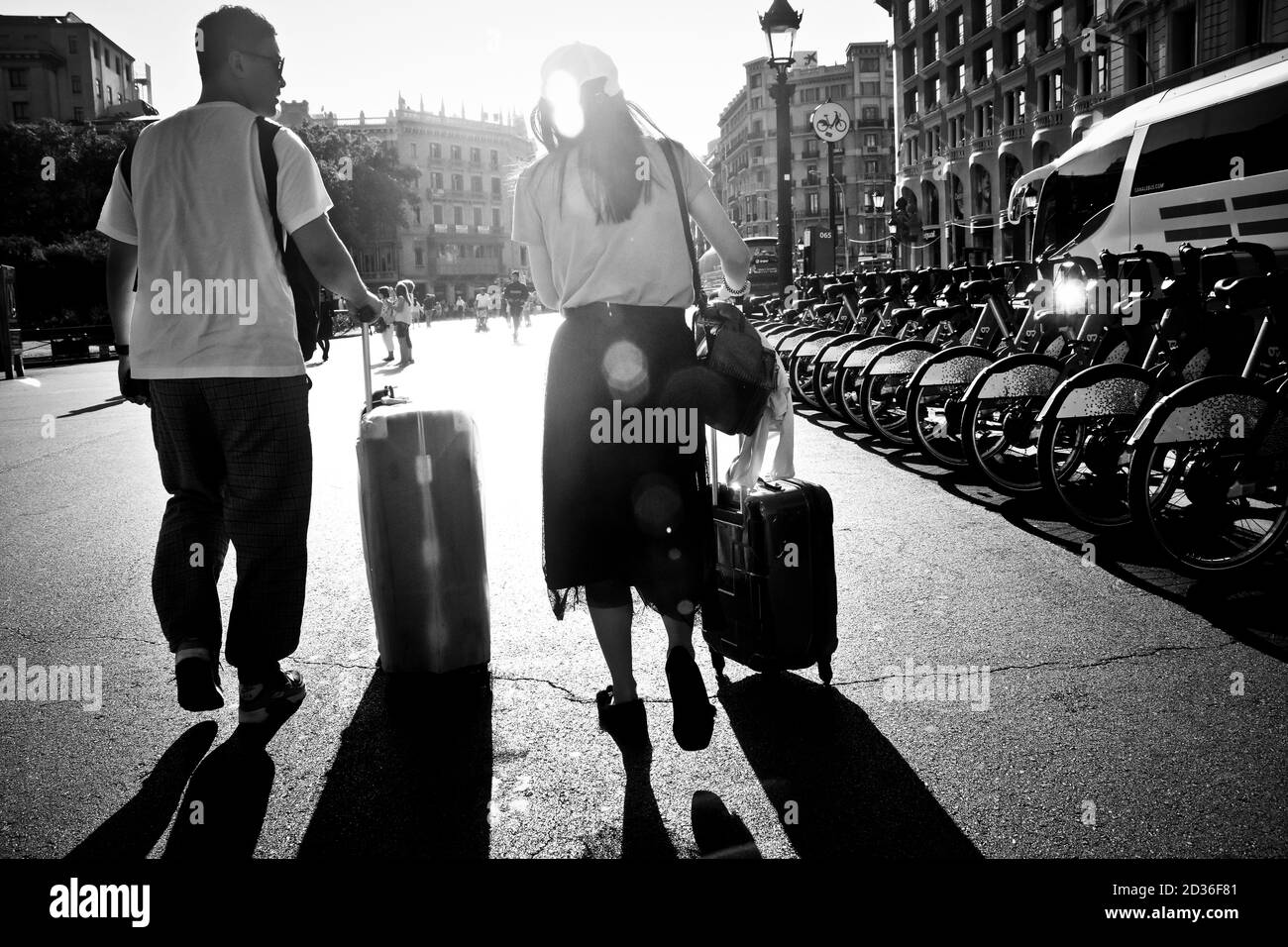 Man and woman walking in a street with their wheeled suitcases. Stock Photo
