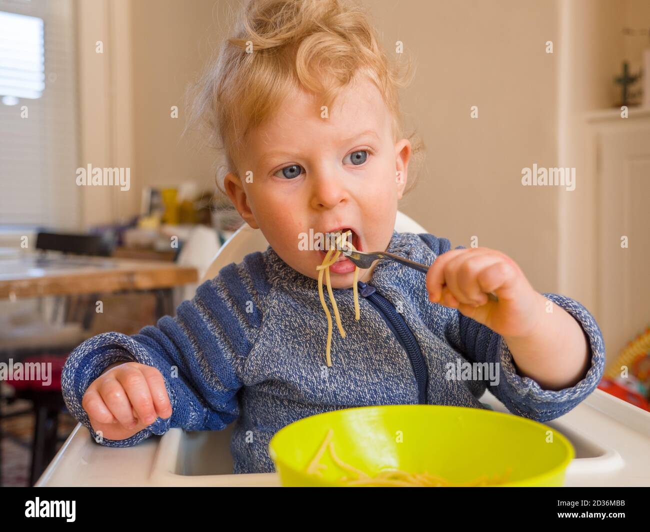 One year old baby boy eating spaghetti with cutlery at home Stock Photo