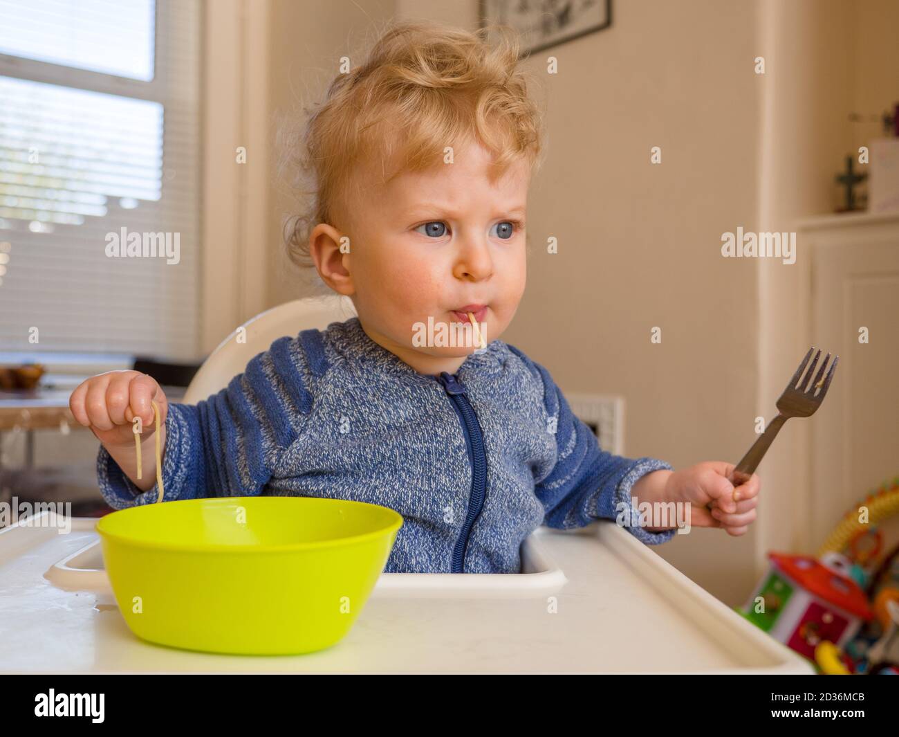 One year old baby boy eating spaghetti with cutlery at home Stock Photo