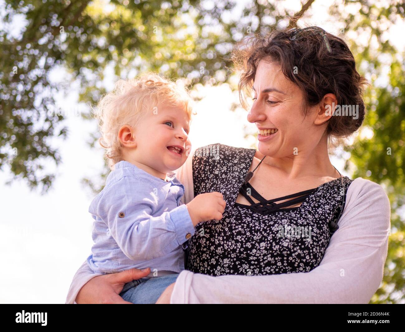 Proud and happy mother smiling and showing her love for her one year old infant baby boy held in her arms outdoors Stock Photo
