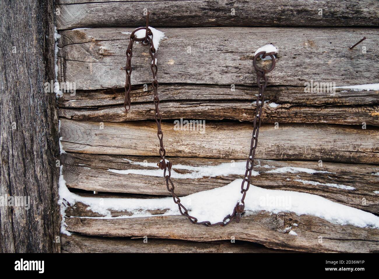 background of old wooden logs with snow and hanging rusty chain Stock Photo