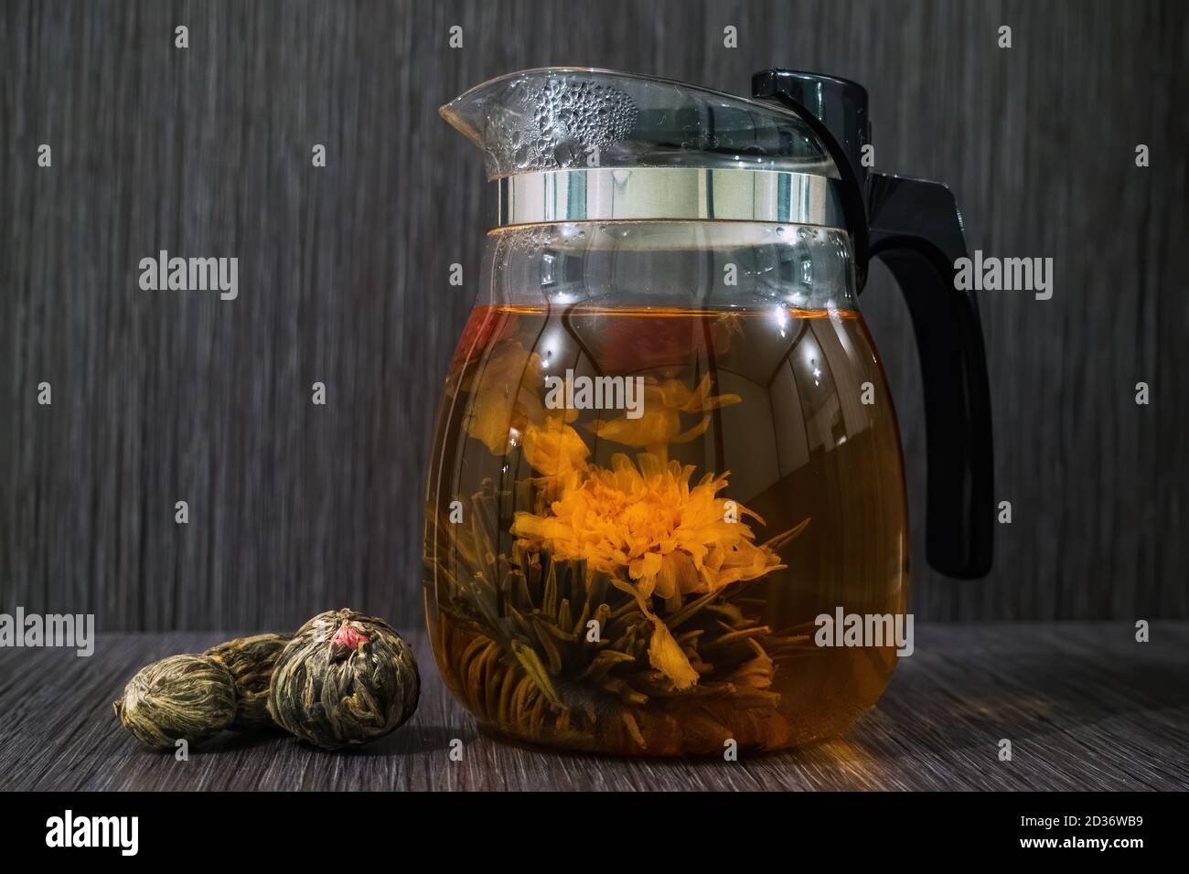 Blooming tea flower in glass teapot and dry flowering tea balls on brown wooden background Stock Photo