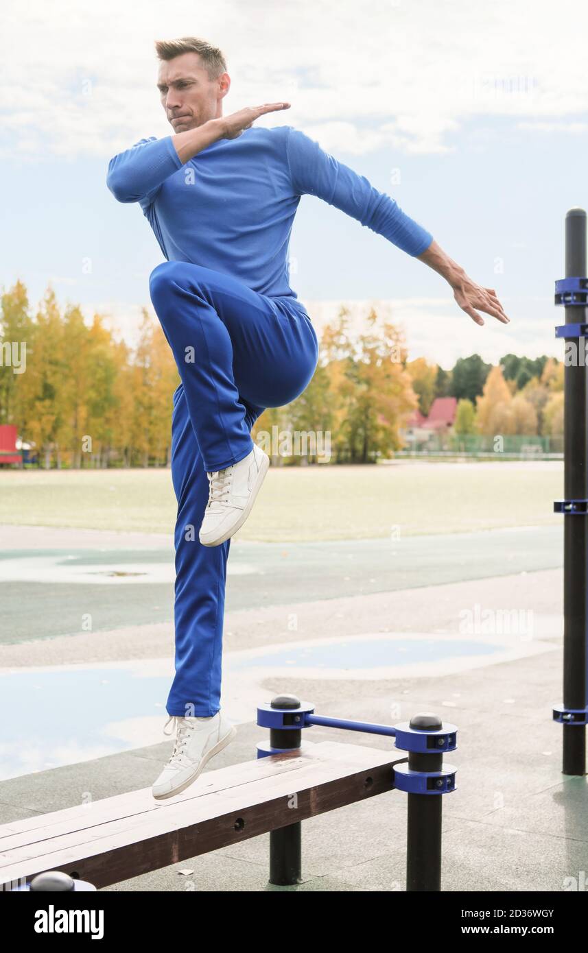 Sporty man workout on open air sports ground. Jump on a bench exercise. Guy wearing blue outfit doing daily exercises in autumn stadium. Active lifestyle. Outdoors training Stock Photo Alamy