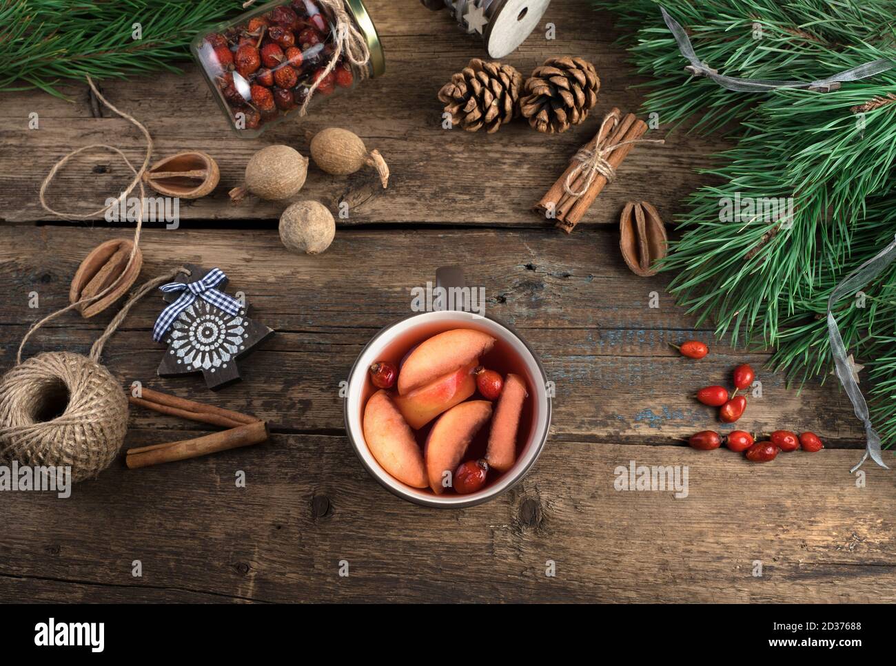 A Cup of mulled wine with fruit, berries and cinnamon on a wooden background with pine branches and Christmas toys. Stock Photo