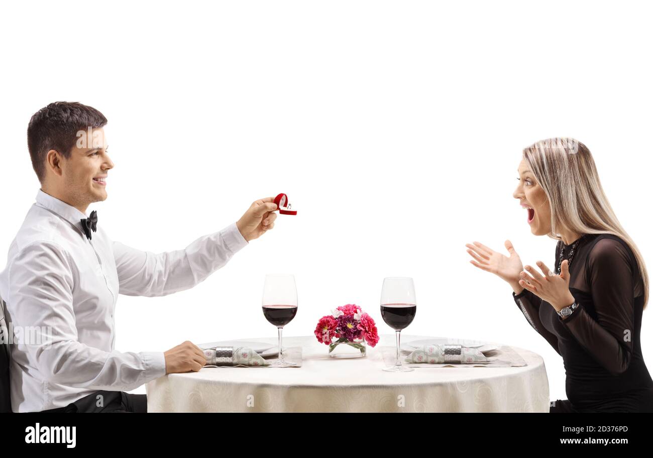 Man proposing a marriage with a ring to a woman at a restaurant table isolated on white background Stock Photo