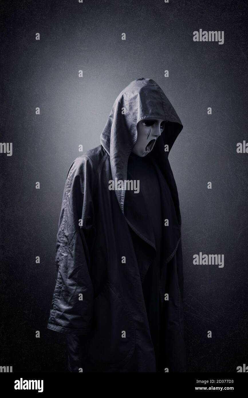 Scary figure with mask in hooded cloak in the dark Stock Photo