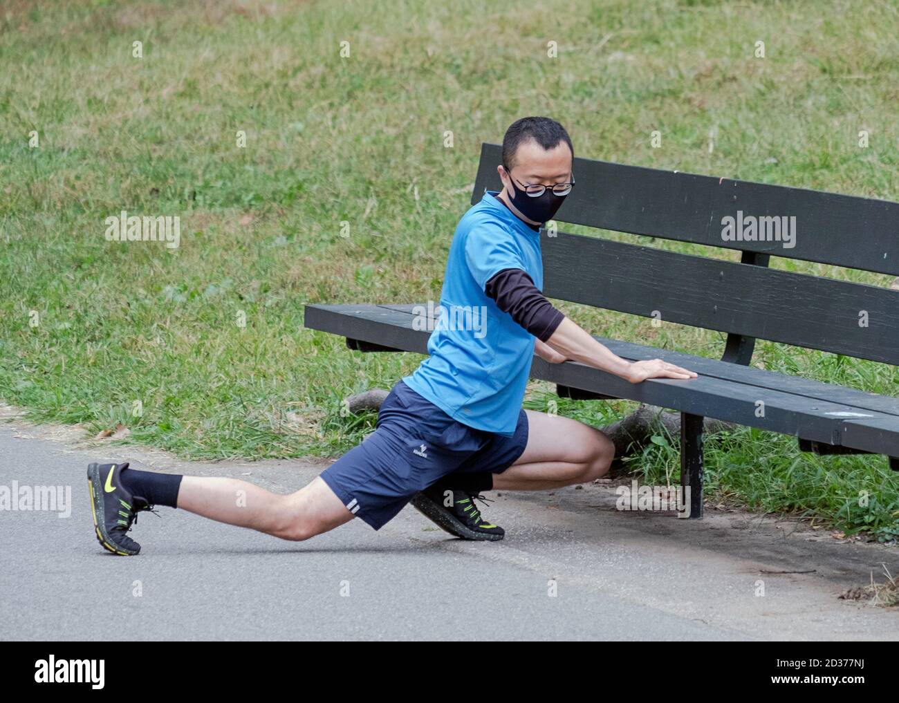 An Asian American man stretches his legs while leaning on a park bench. In Kissena Park, Flushing, Queens, New York City. Stock Photo