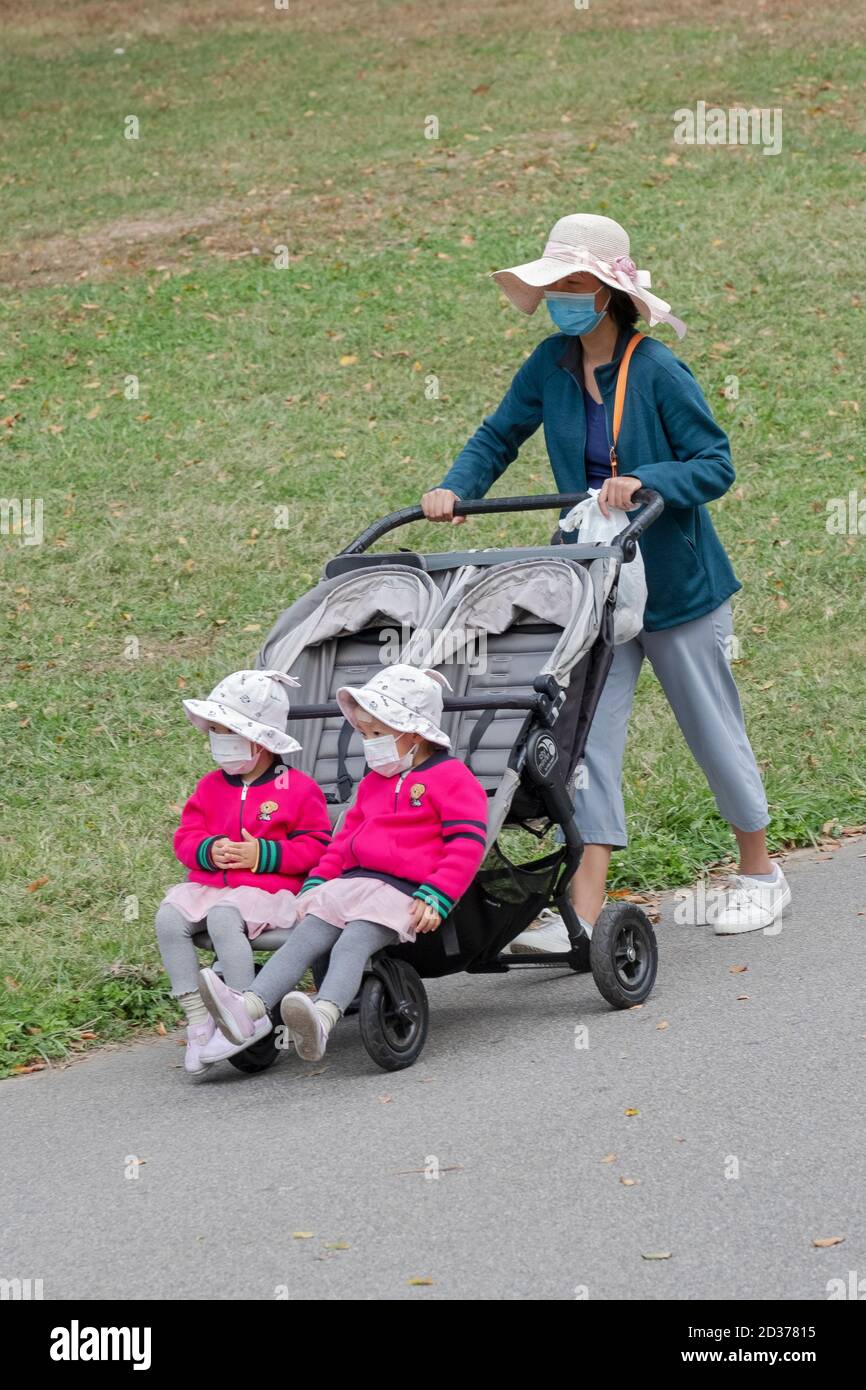 An ASian American woman pushes her daughters in a stroller. Both are dressed identically and are likely twins. In Queens, New York. Stock Photo