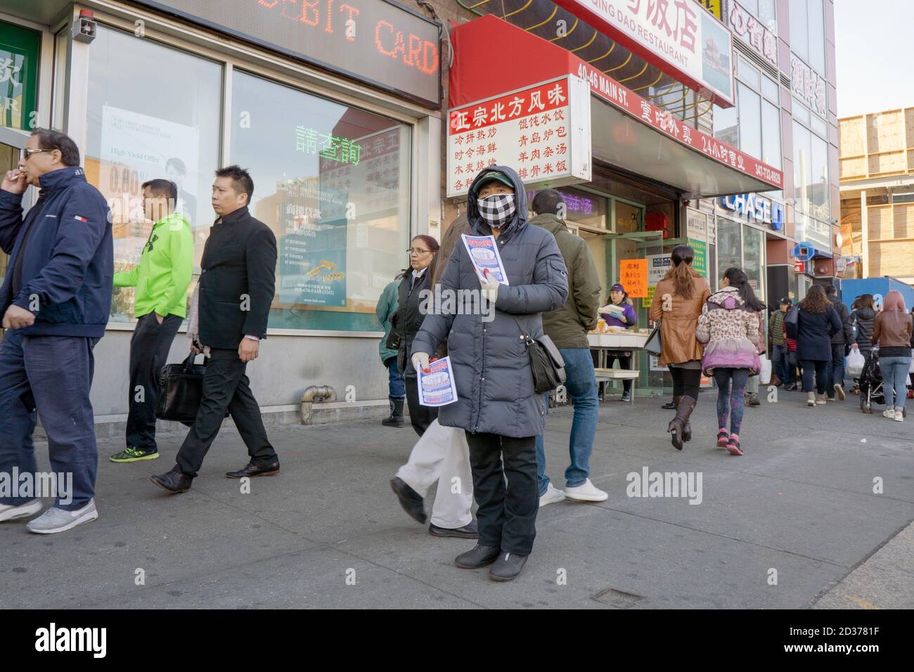 A Chinese American woman in a mask hands out advertising flyers on Main St. in Chinatown, Flushing, NY. In 2016, before the pandemic. Stock Photo