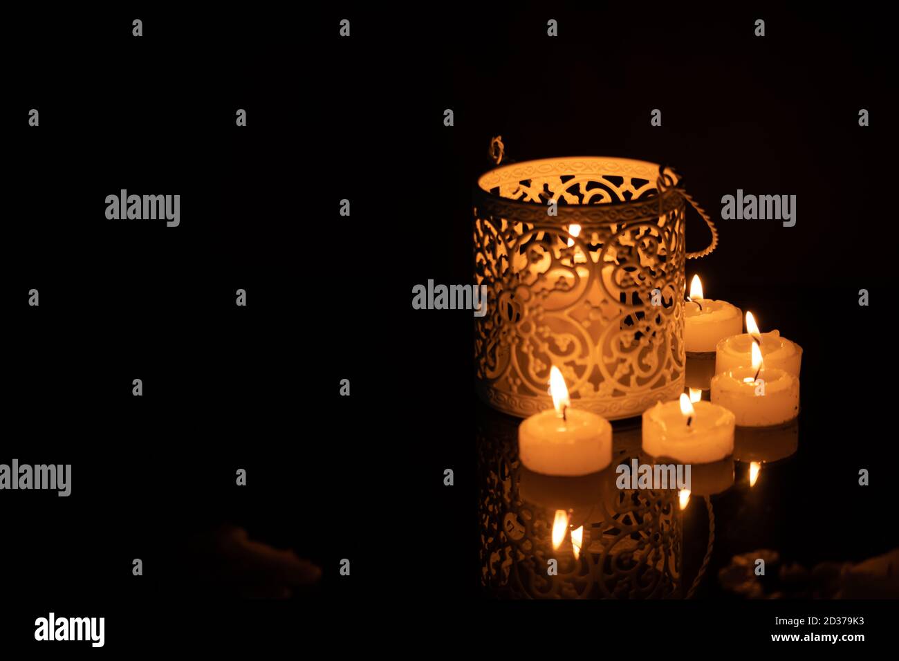 Intrincate metal candle holder with a lighting scented candle are displayed on the blak stone table in the dark living room. Stock Photo