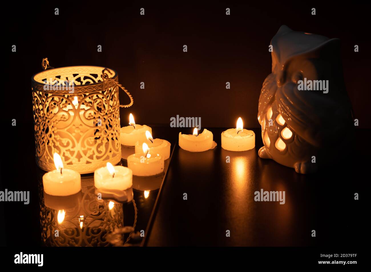 Intrincate metal candle holder with a lighting scented candle are displayed on the blak stone table in the dark living room. Stock Photo