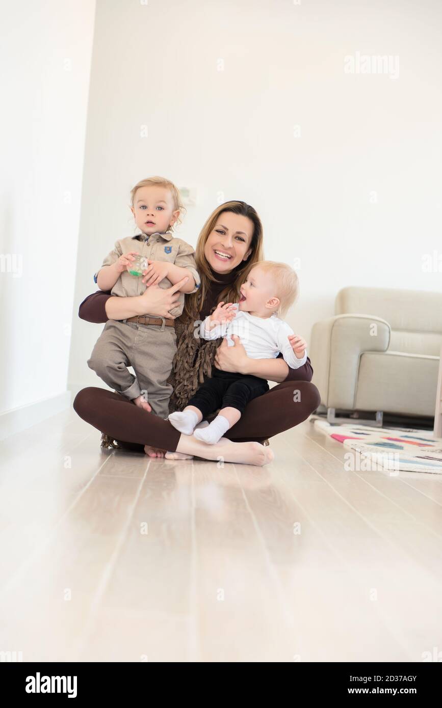 Happy mother sitting on the floor with her two babies and playing Stock ...