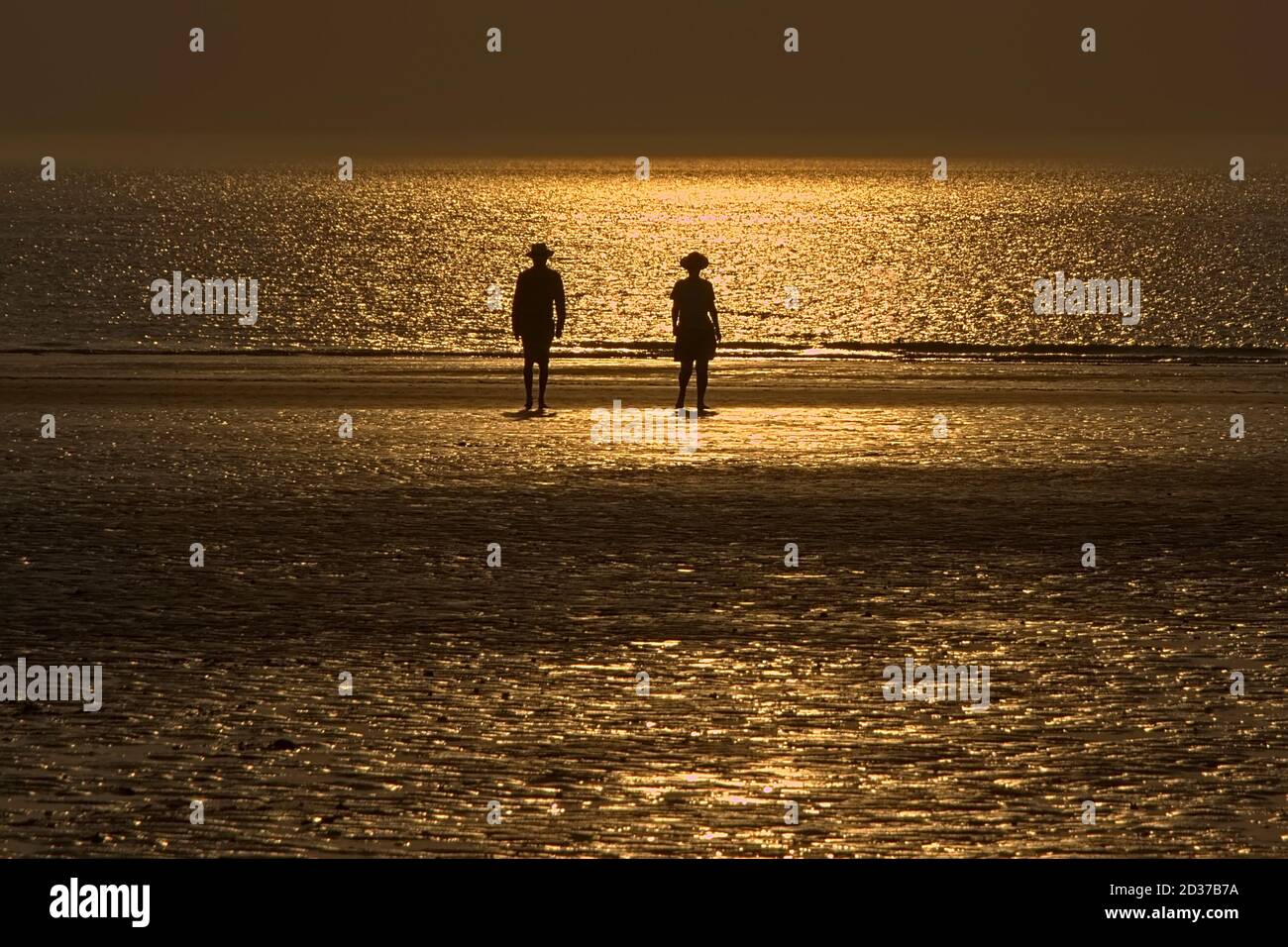Silhouettes of two people walking on the north sea beach with reflection of  the setting sun in the water and sand Stock Photo - Alamy, image size:1300x956
