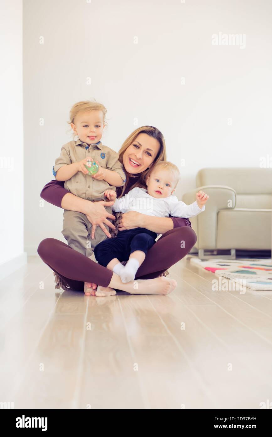 Happy mother sitting on the floor with her two babies and playing Stock ...
