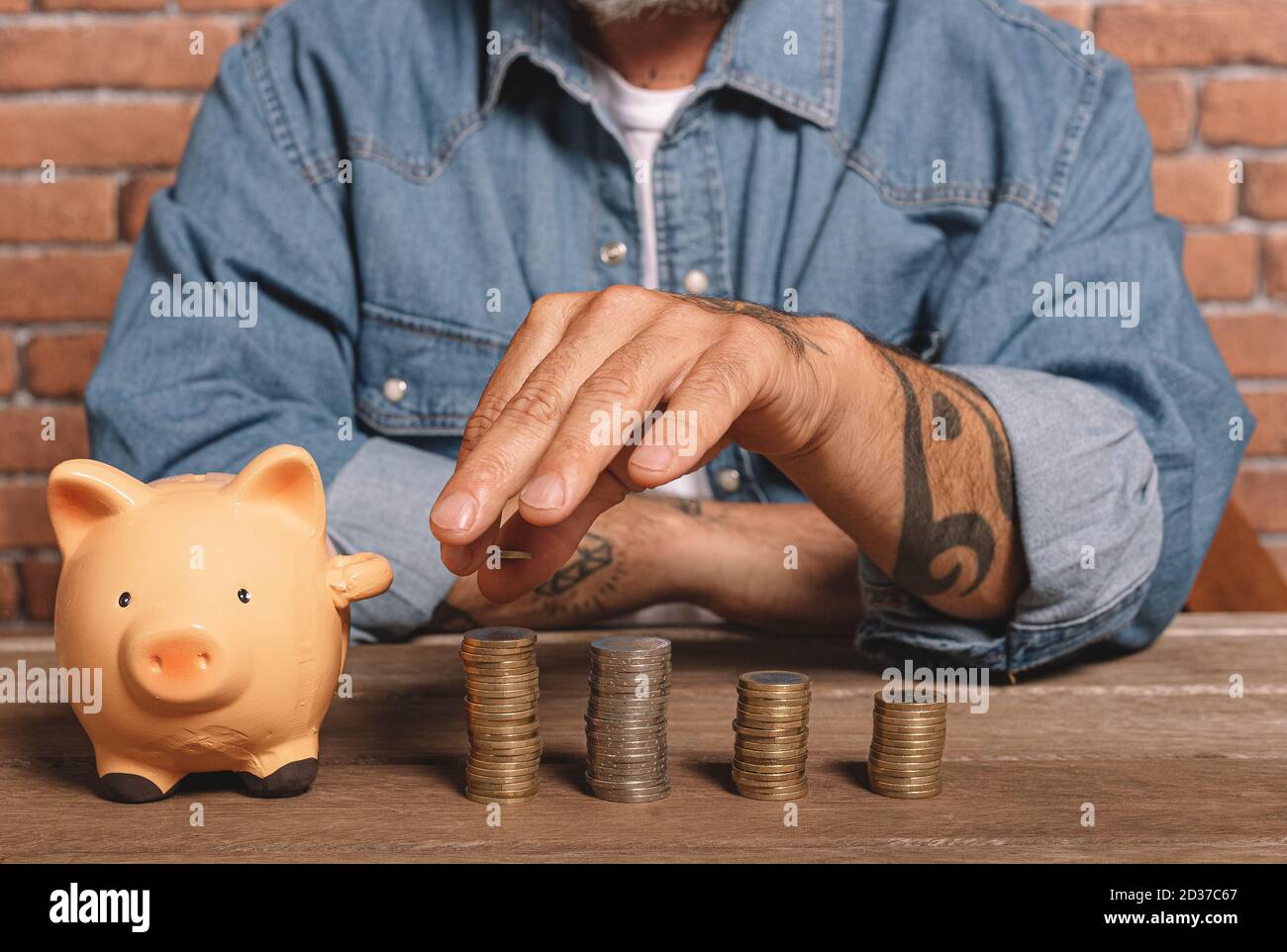 Hipster man stacks coins with a pig piggy bank on the table to save money and financial concept. Stock Photo