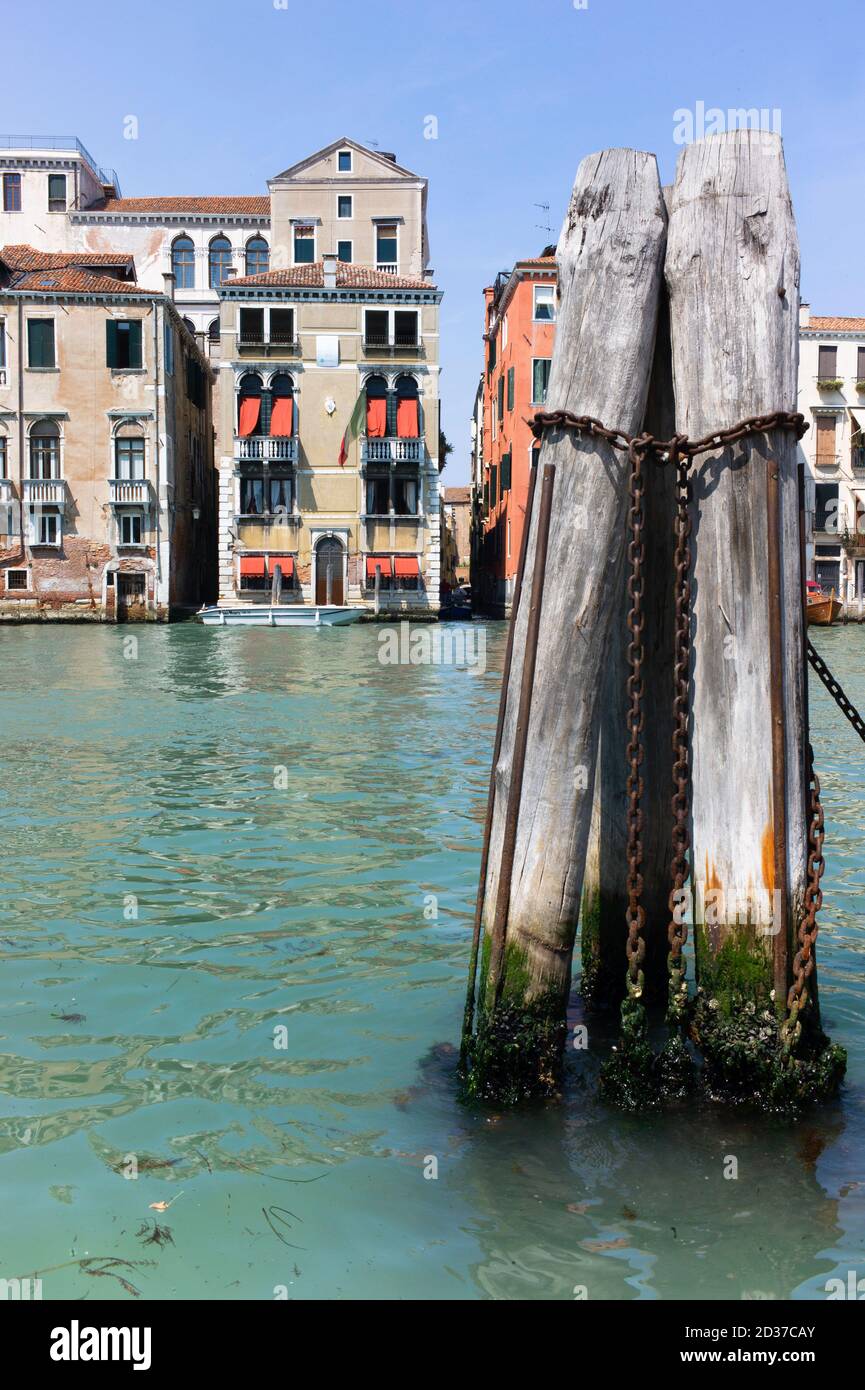 Venice with historic buildings in on the canal in the background. In the front a wooden bollard with rusty chains in the water. Vertical image Stock Photo
