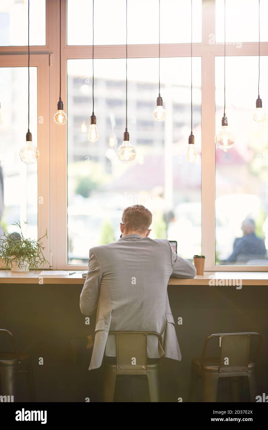 Rear view of a businessman or male freelancer sitting in cafe and working remotely, using laptop Stock Photo