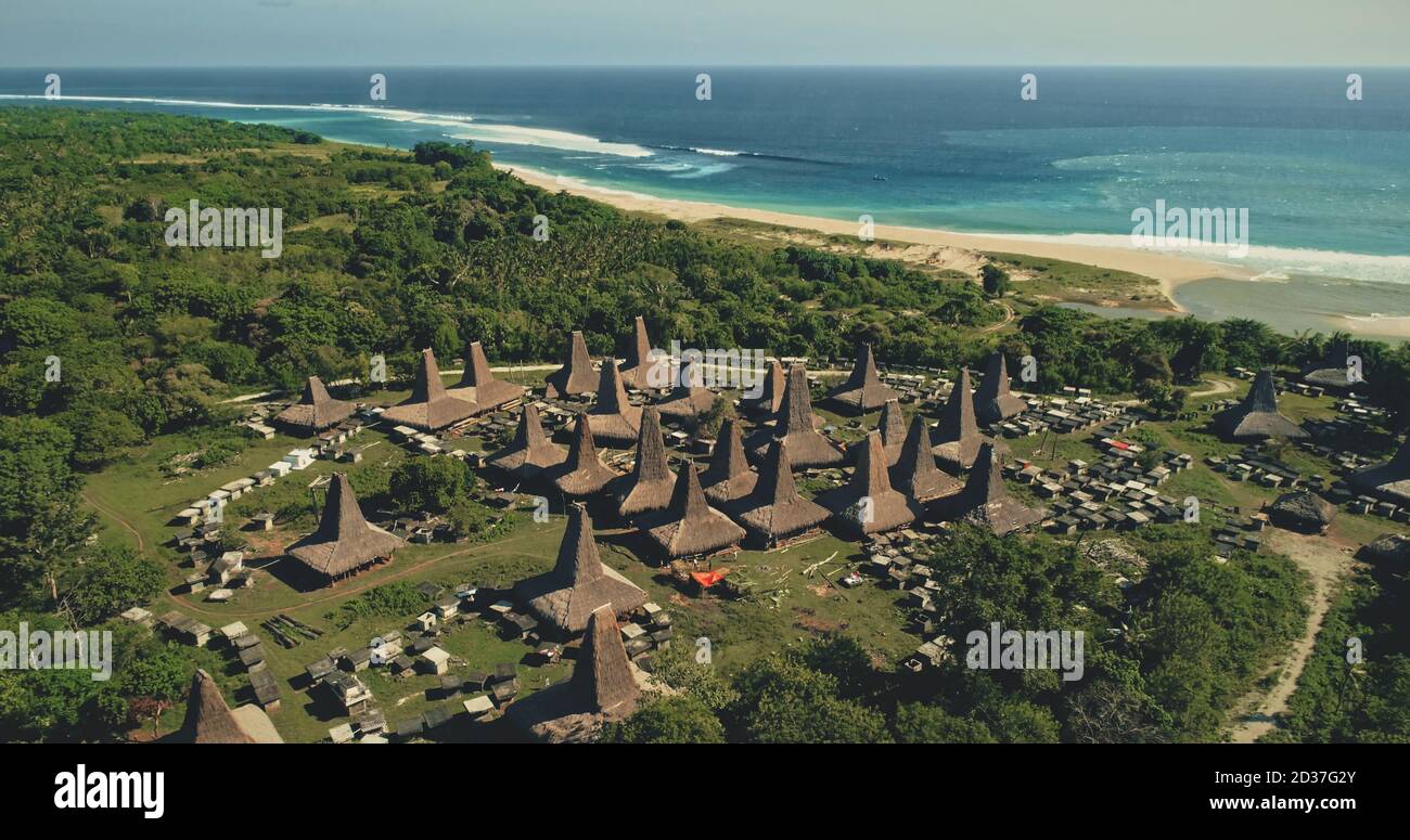 Amazing seaside traditional village with unique designed roofs houses aerial view. Indonesia tourist attraction at green valley with tropic trees near ocean bay. Cinematic scenic landscape drone shot Stock Photo