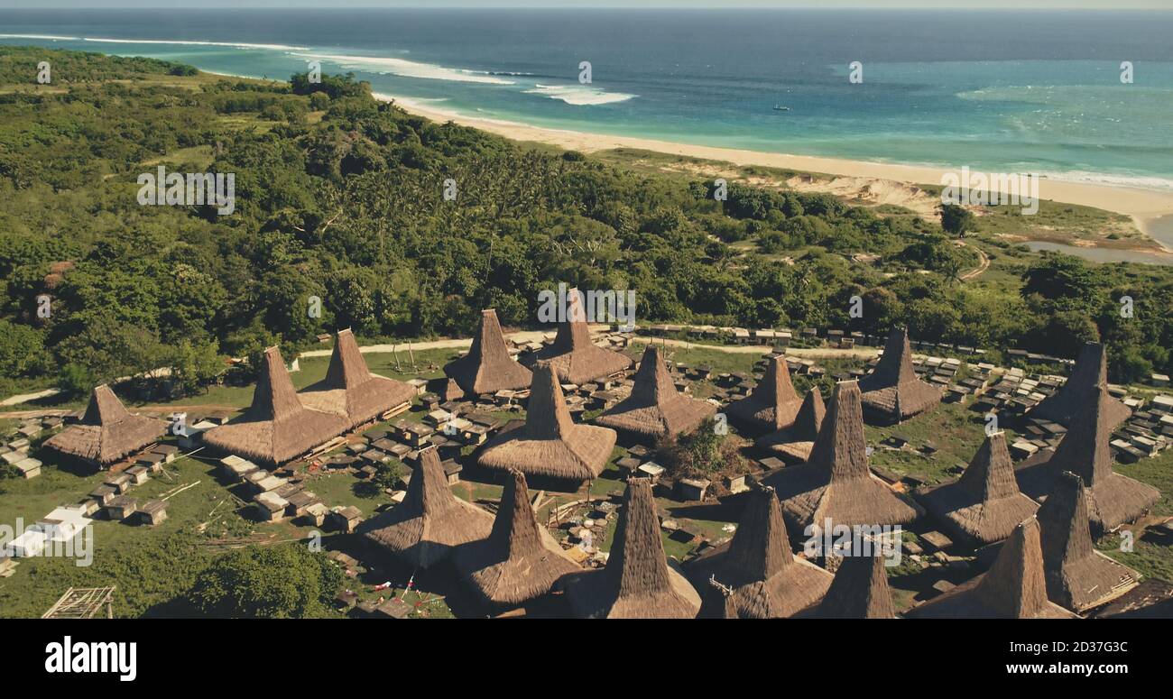 Seaside long-held tradition village with unique ornately roofs houses aerial view. Indonesia landmark at green ocean coast with sand beach. Greenery countryside landscape of Sumba Island, Asia Stock Photo