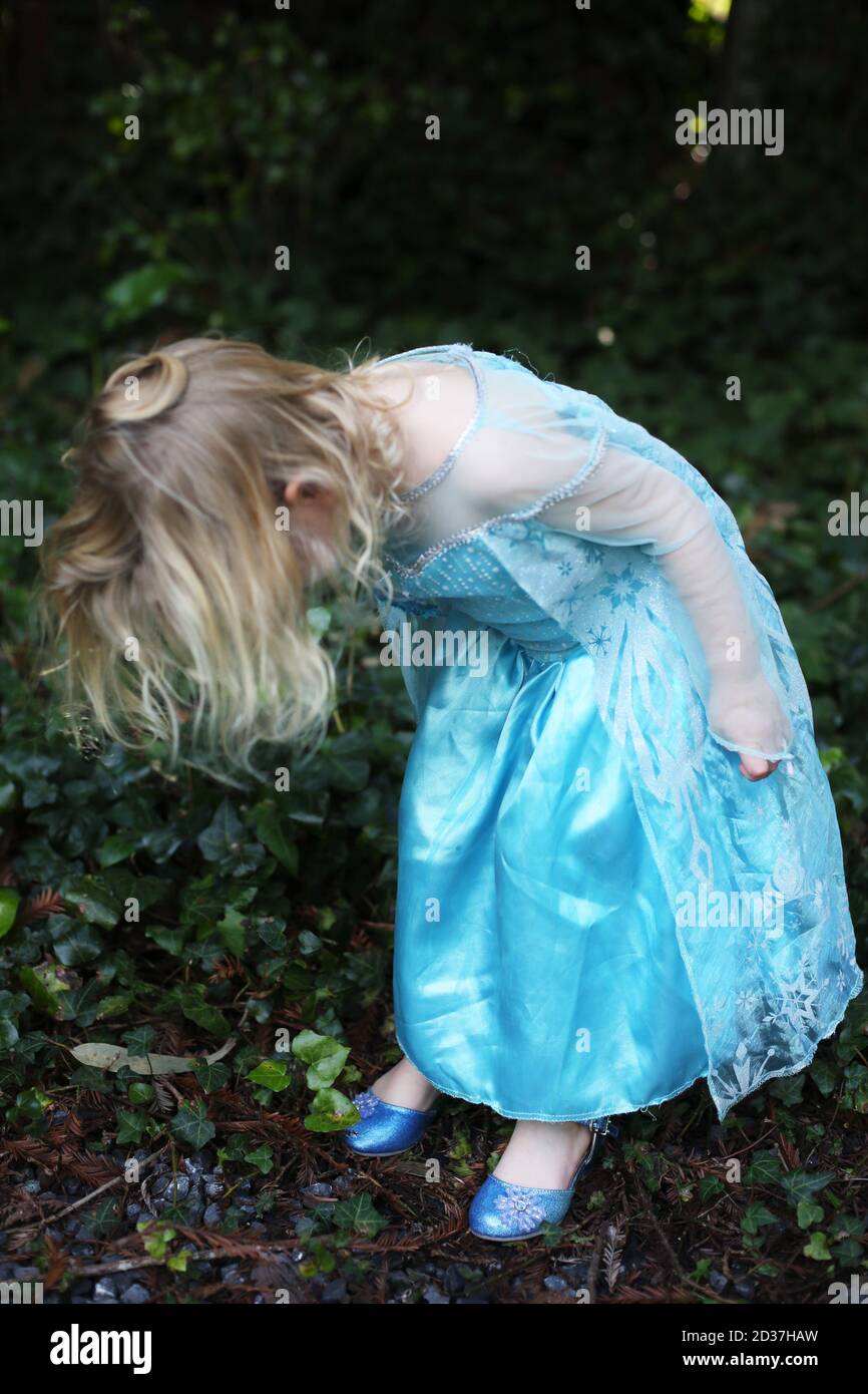 A little girl in a blue dress looking down at her blue satin shoes. Stock Photo