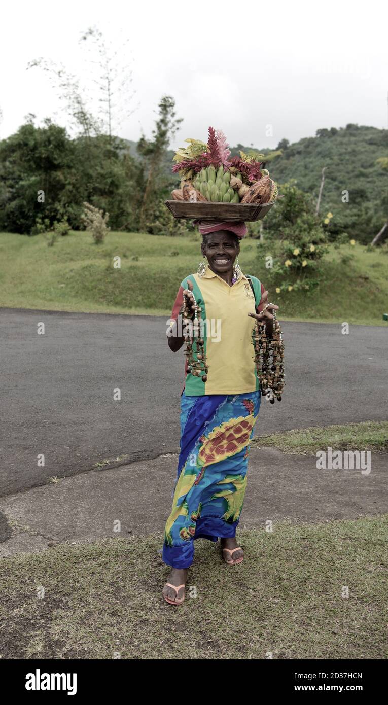 st.Georges, Grenada-November 27, 2015: old afro american woman with smiling face selling fruits in basket on head and beads Stock Photo