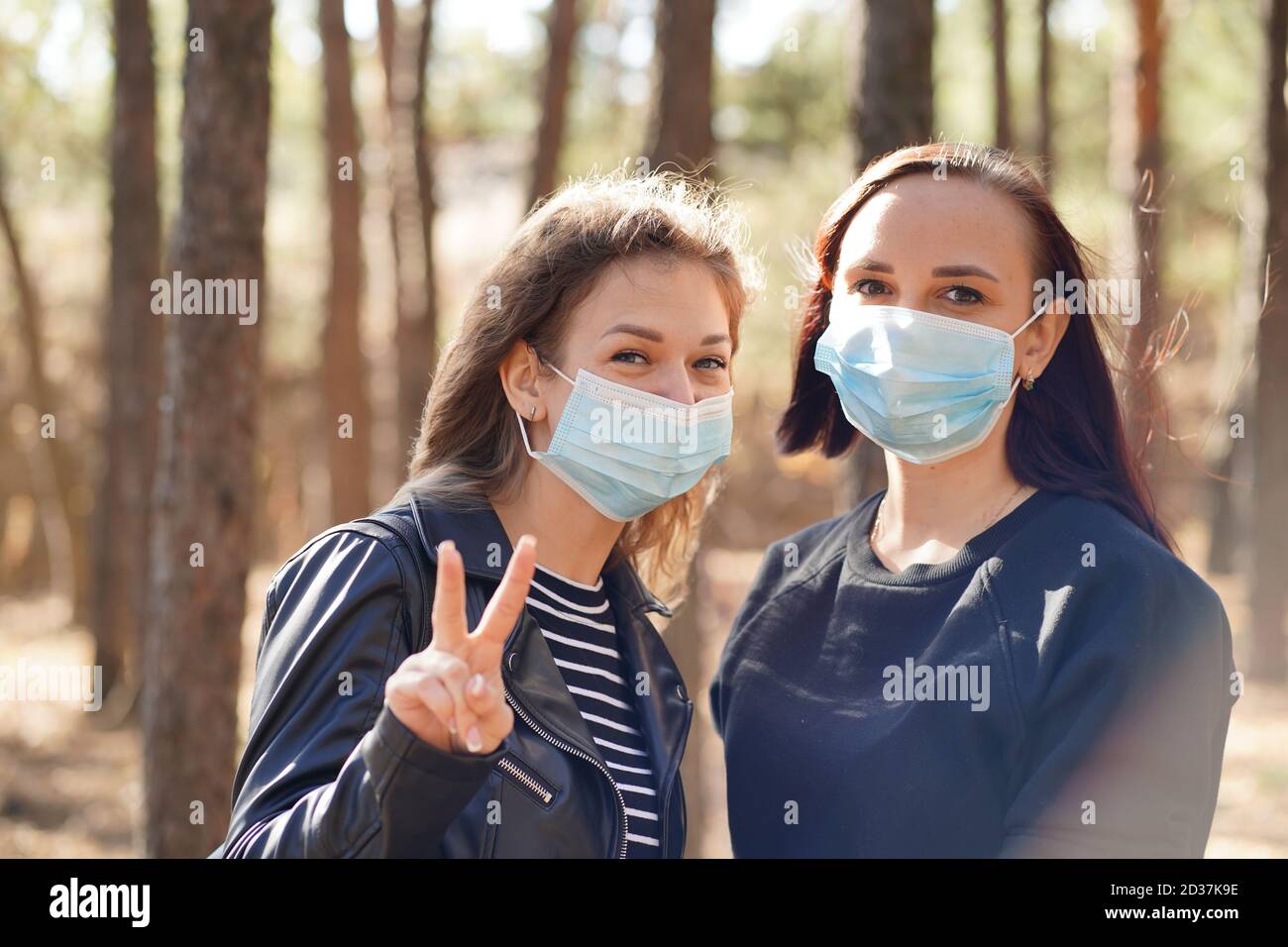 Two young women in medical masks look at camera in wood. Close up of ...