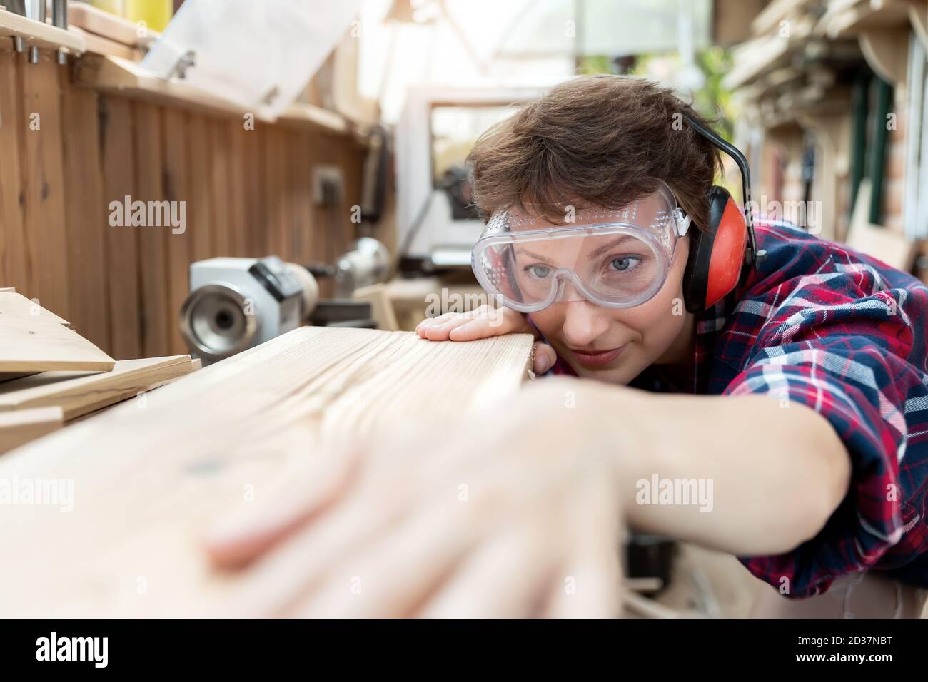 Young attractive 30-40 professional female carpenter looking grinding raw wood with sandpaper in carpentry diy workshop. Feminine women equality Stock Photo
