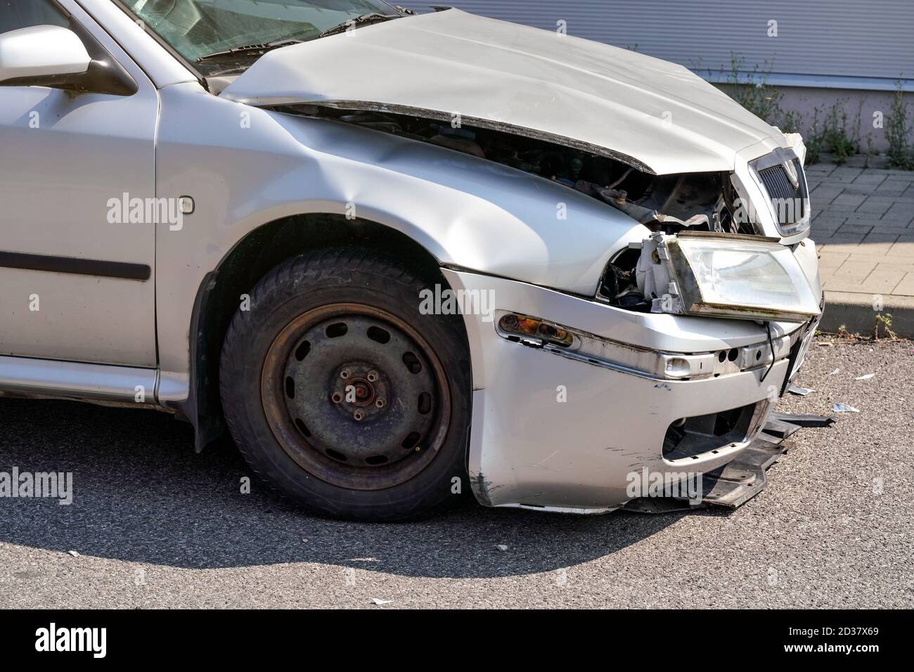 Silver car with its front crashed, plates dented and broken on asphalt road, detail to damaged part Stock Photo