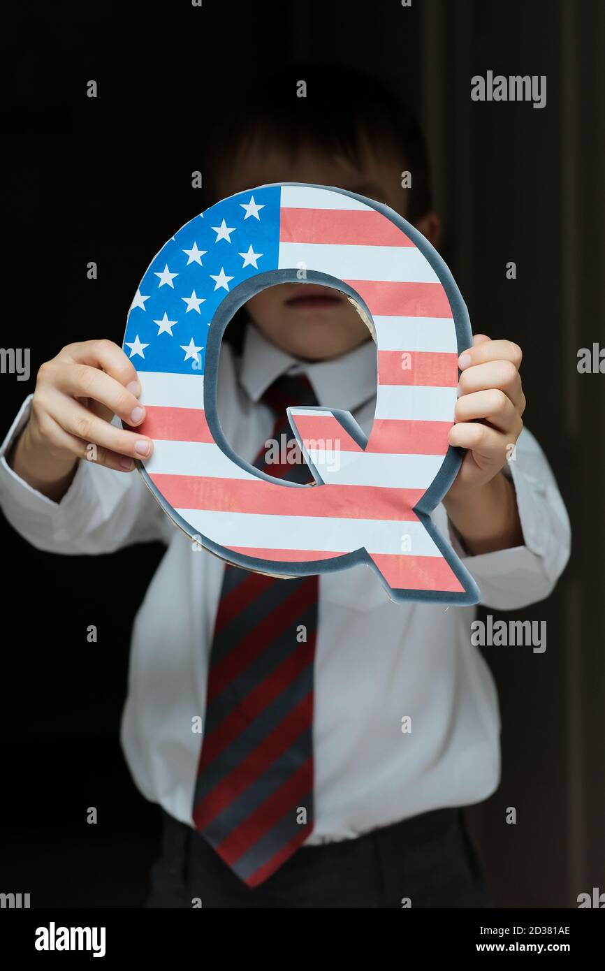 QAnon concept. Q letter with american flag seen in hands of unrecognisable child in blurred background.  Selective focus. Stock Photo