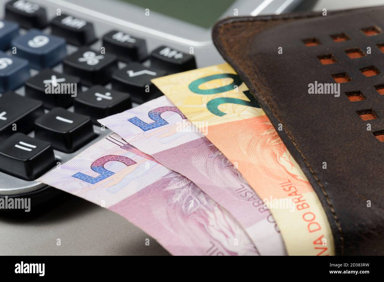 money coming out of wallet with blurred pocket calculator in the background. Stock Photo
