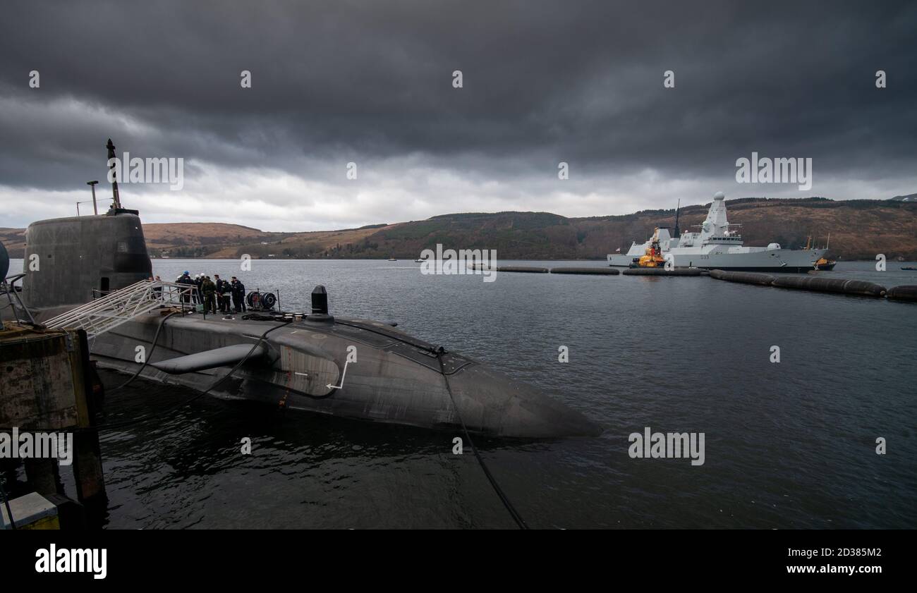 An Astute class submarine alongside the Faslane submarine base in Scotland with a Type 45 destroyer leaving harbour. Stock Photo