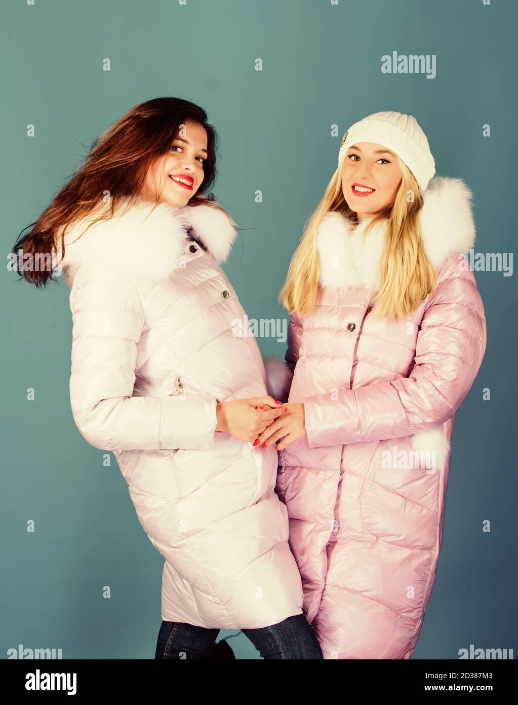 Fashion friends. Winter season. Soft fur. For those wishing stay modern. Winter  clothes. Women wear down jacket with furry hood. Girls smiling makeup faces wear  winter jackets blue background Stock Photo 