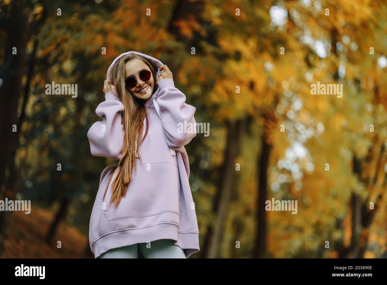 Beautiful happy smiling young woman wearing pink hoodie walking in autumn park. Season and people concept. Stock Photo