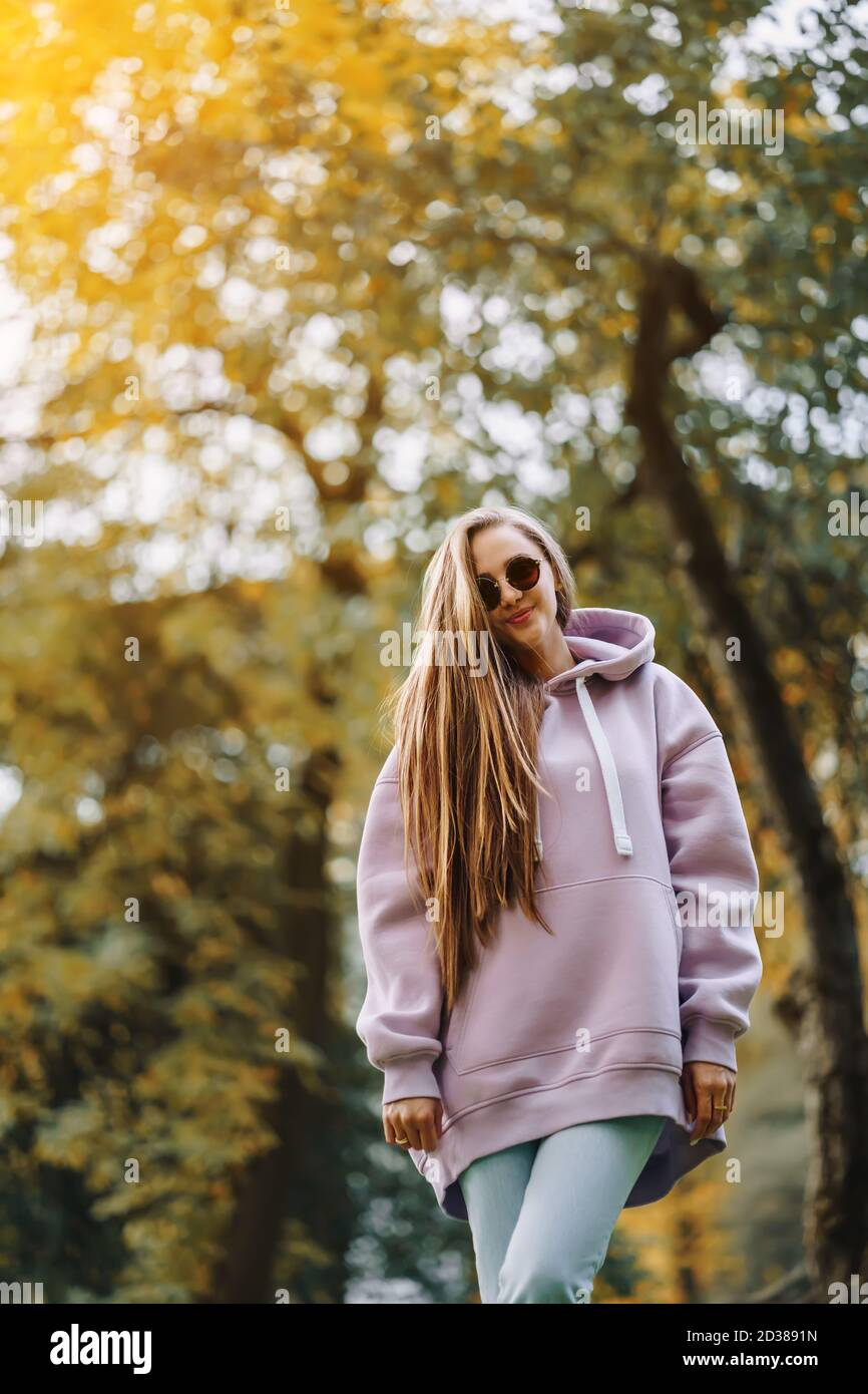 Beautiful happy smiling young woman wearing pink hoodie walking in autumn park. Season and people concept. Stock Photo