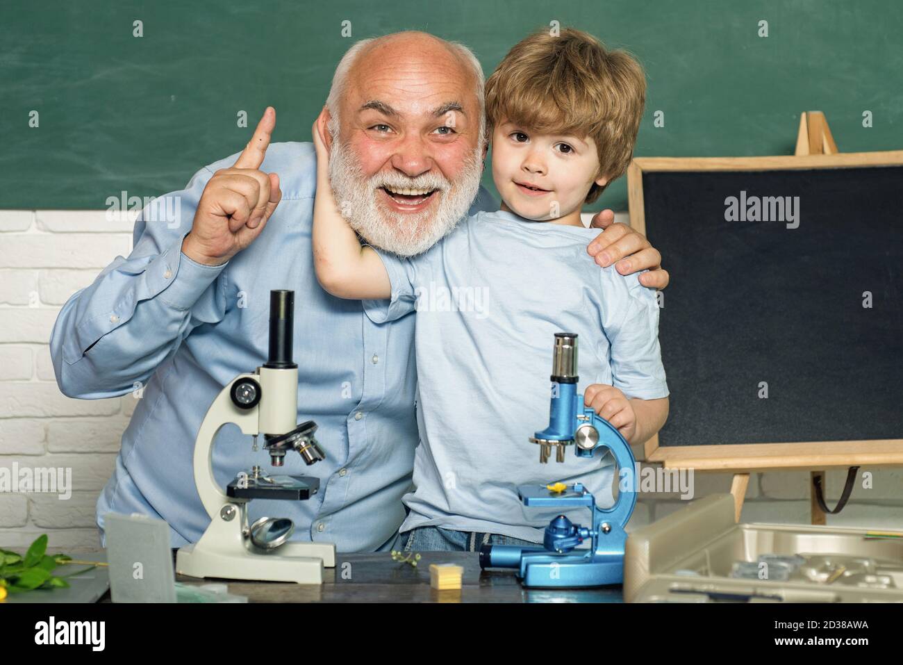 Friendly teacher in classroom near blackboard desk. Lab microscope and
