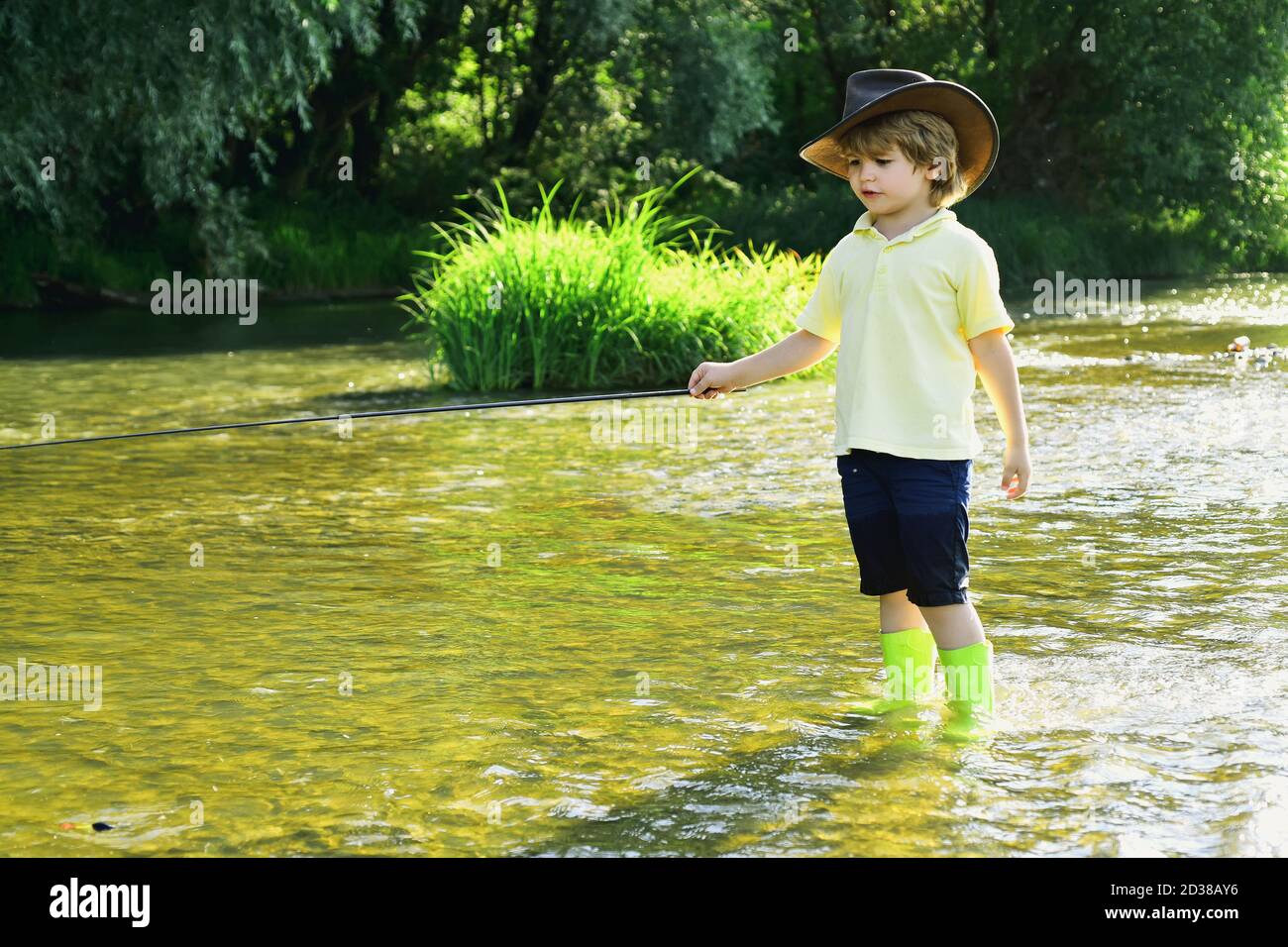 Young boy fishing in a forest river. Boy in yellow shirt with a