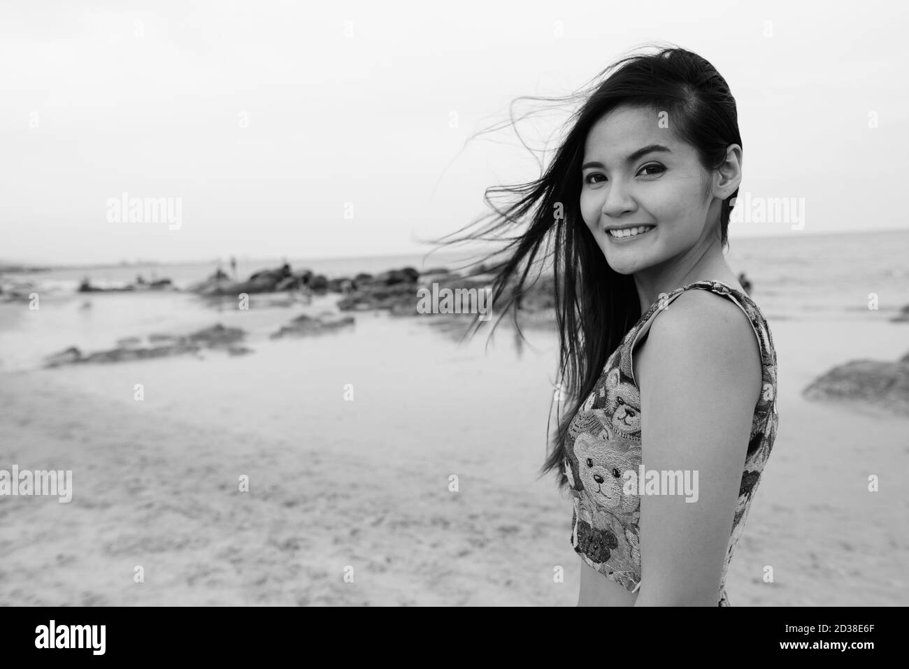 Young happy beautiful Asian woman smiling at the public beach of Hua Hin in Thailand Stock Photo
