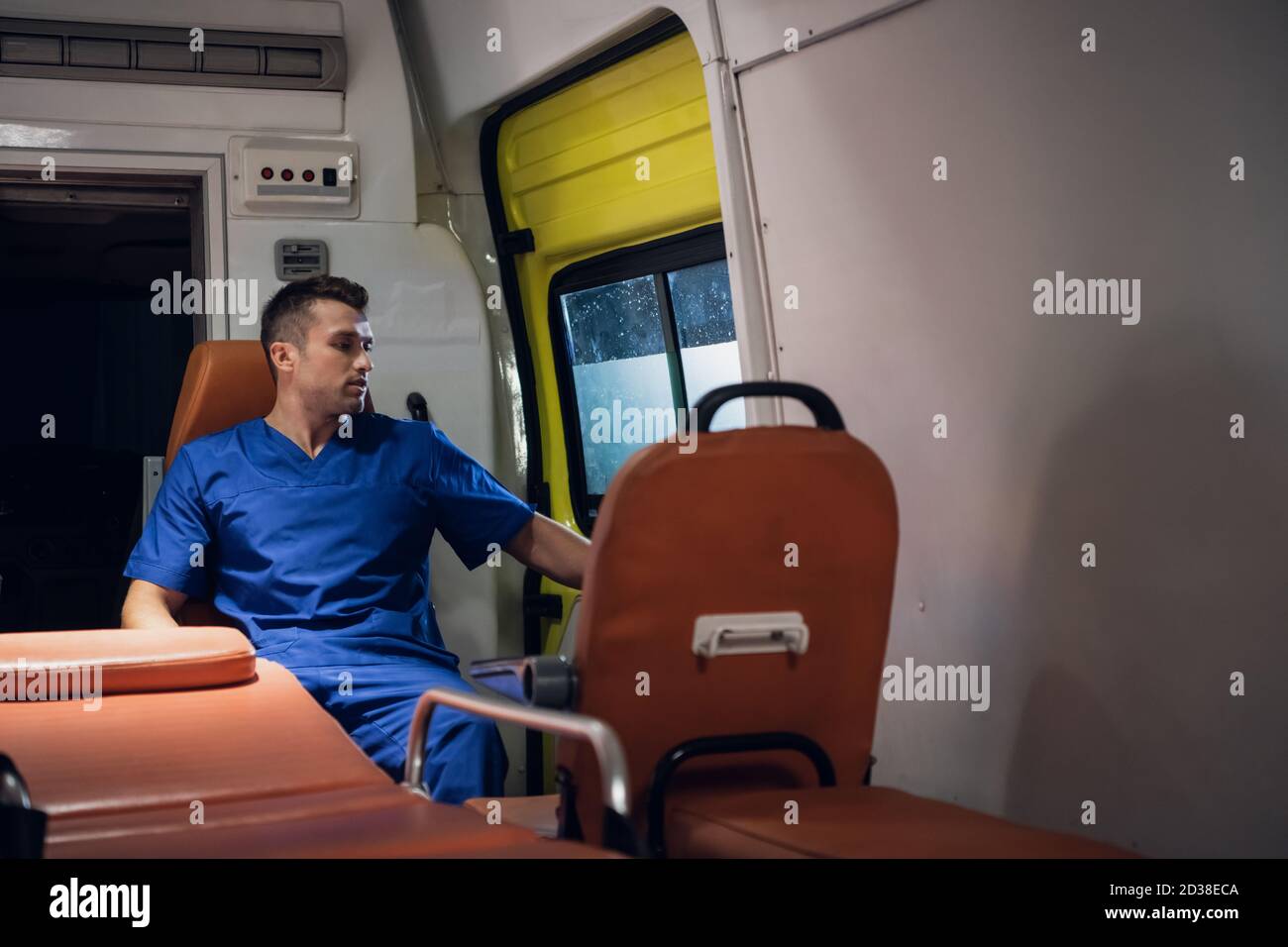 Man in a medical uniform sitting in an ambulance car and looking through the window Stock Photo