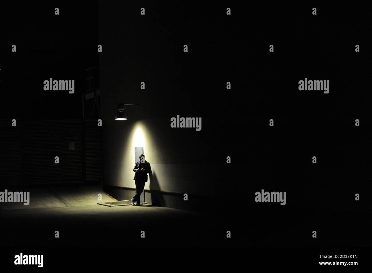 Man leaning against a wall, standing under a street lamp at night ...