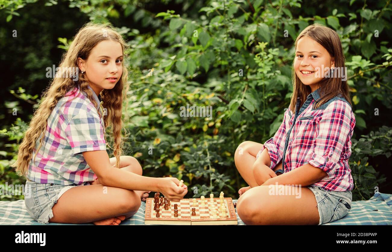 Cognitive development. Intellectual game. Make decision. Smart children. Little girls play chess. Sisters playing chess. Children play chess outdoors nature background. Sport and hobby concept. Stock Photo