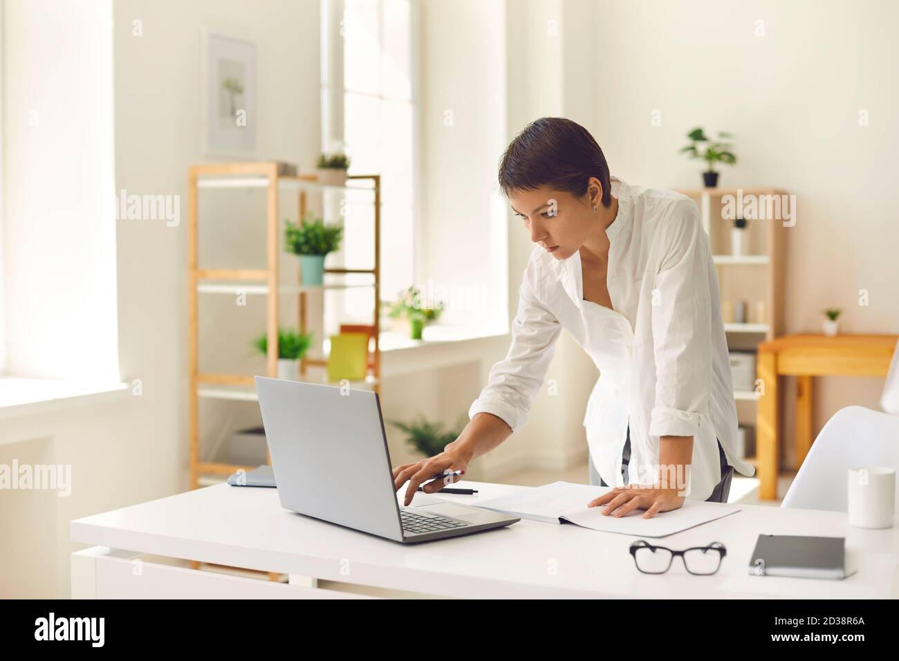 Serious concentrated woman standing at desk in home office and working on  laptop computer Stock Photo - Alamy