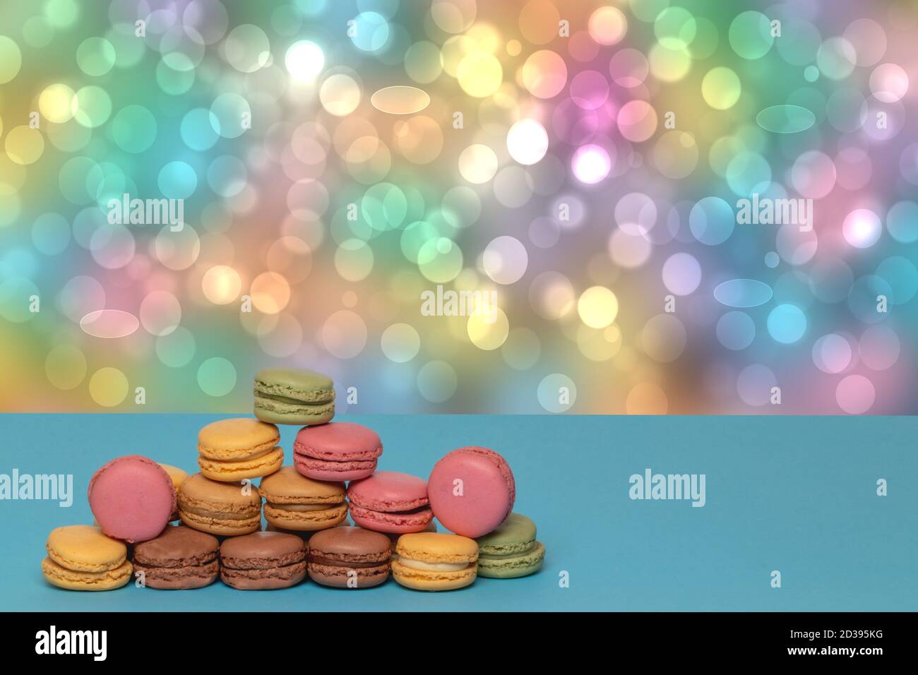 Close-up of colourful French macaroons in shape of a pyramid on a blue table against abstract bright pastel colored background. Advertising bakery or Stock Photo