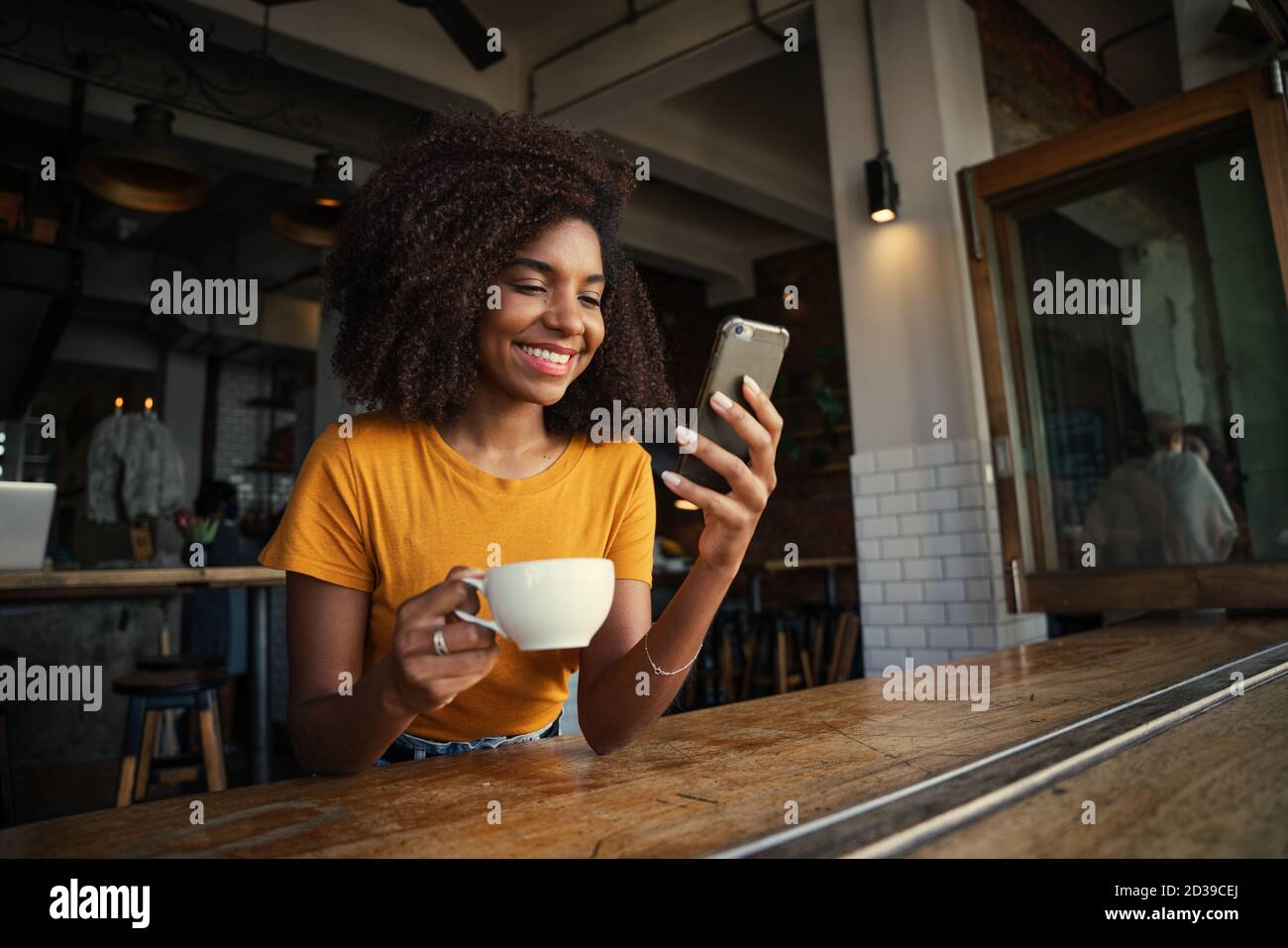 Beautiful African American woman scrolling on smartphone driving coffee in trendy coffee shop. Stock Photo