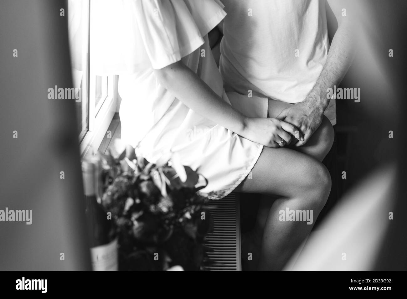 Cropped image of the groom hugging the bride sitting on the windowsill in the morning before the meeting. Wedding details. Black and white photo. Morn Stock Photo