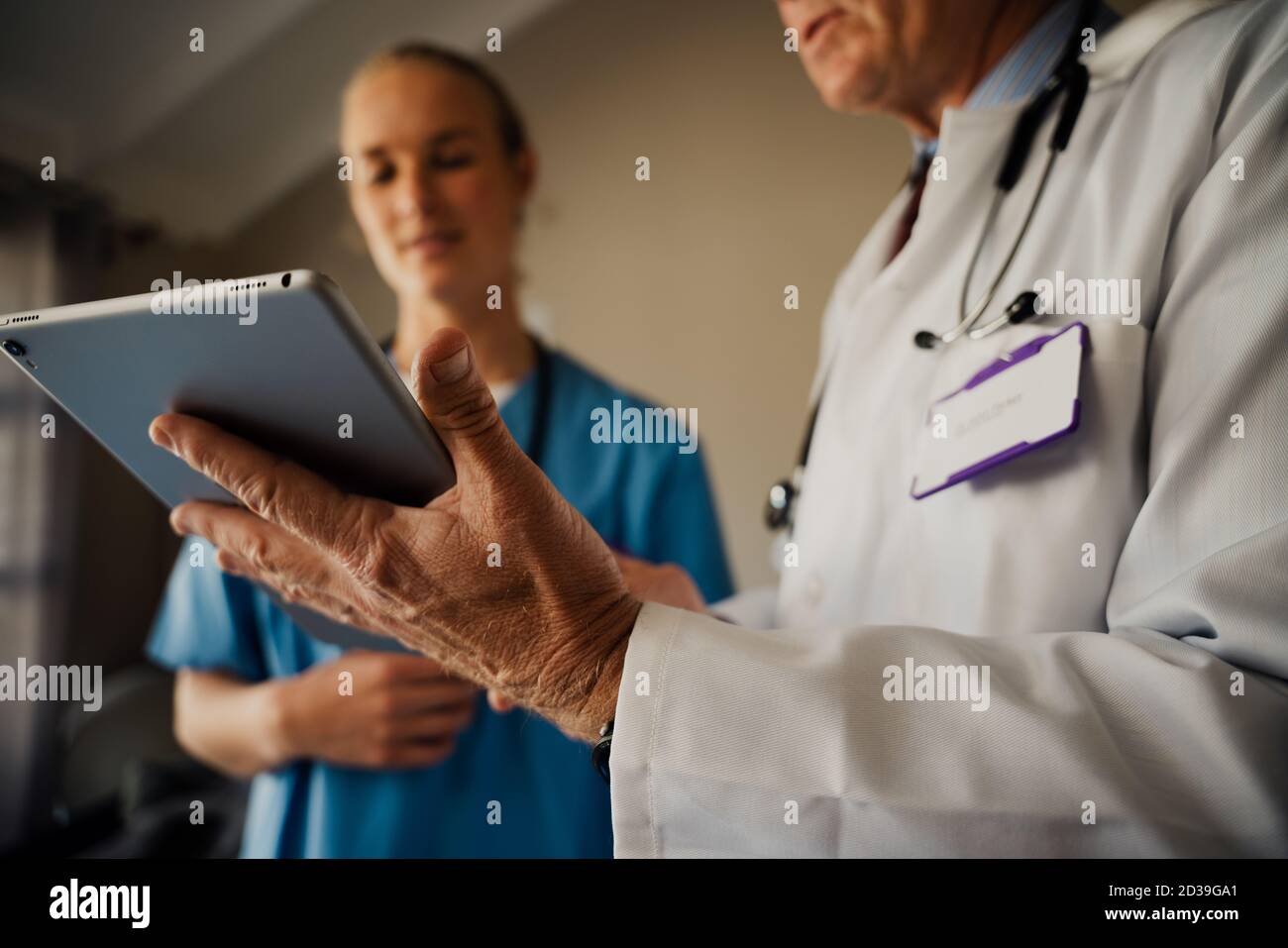 Close up of male doctor holding digital tablet while female intern listens to instructions standing in organised office Stock Photo
