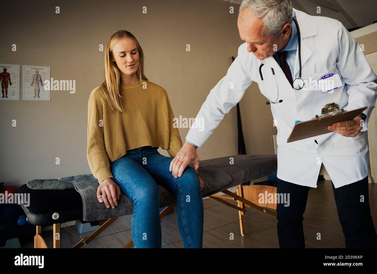 male doctor in scrubs examines young female patients knee Stock Photo