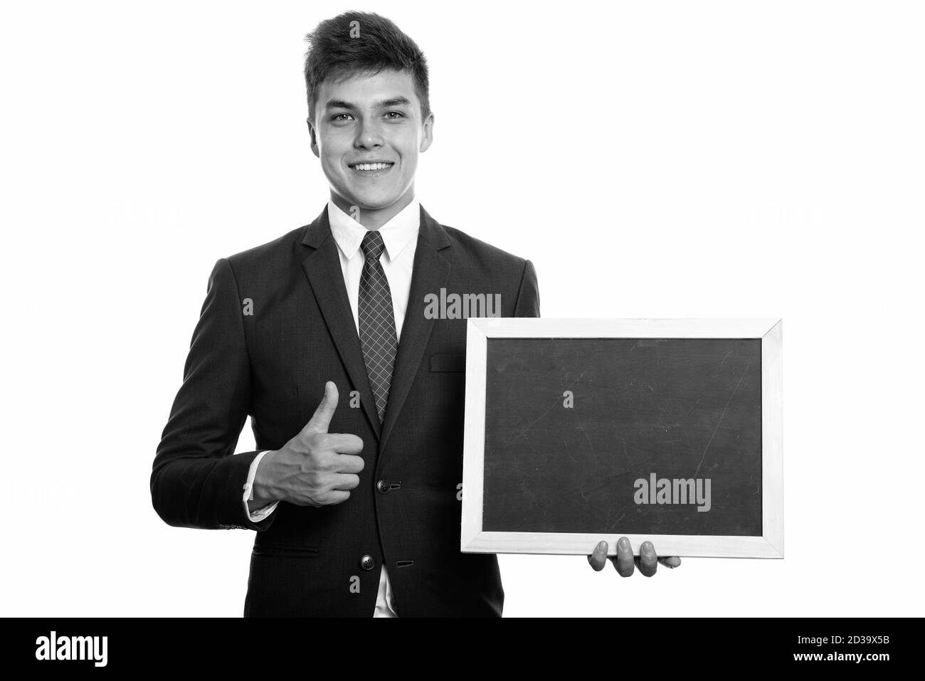 Young happy businessman smiling while holding blank blackboard and giving thumb up Stock Photo
