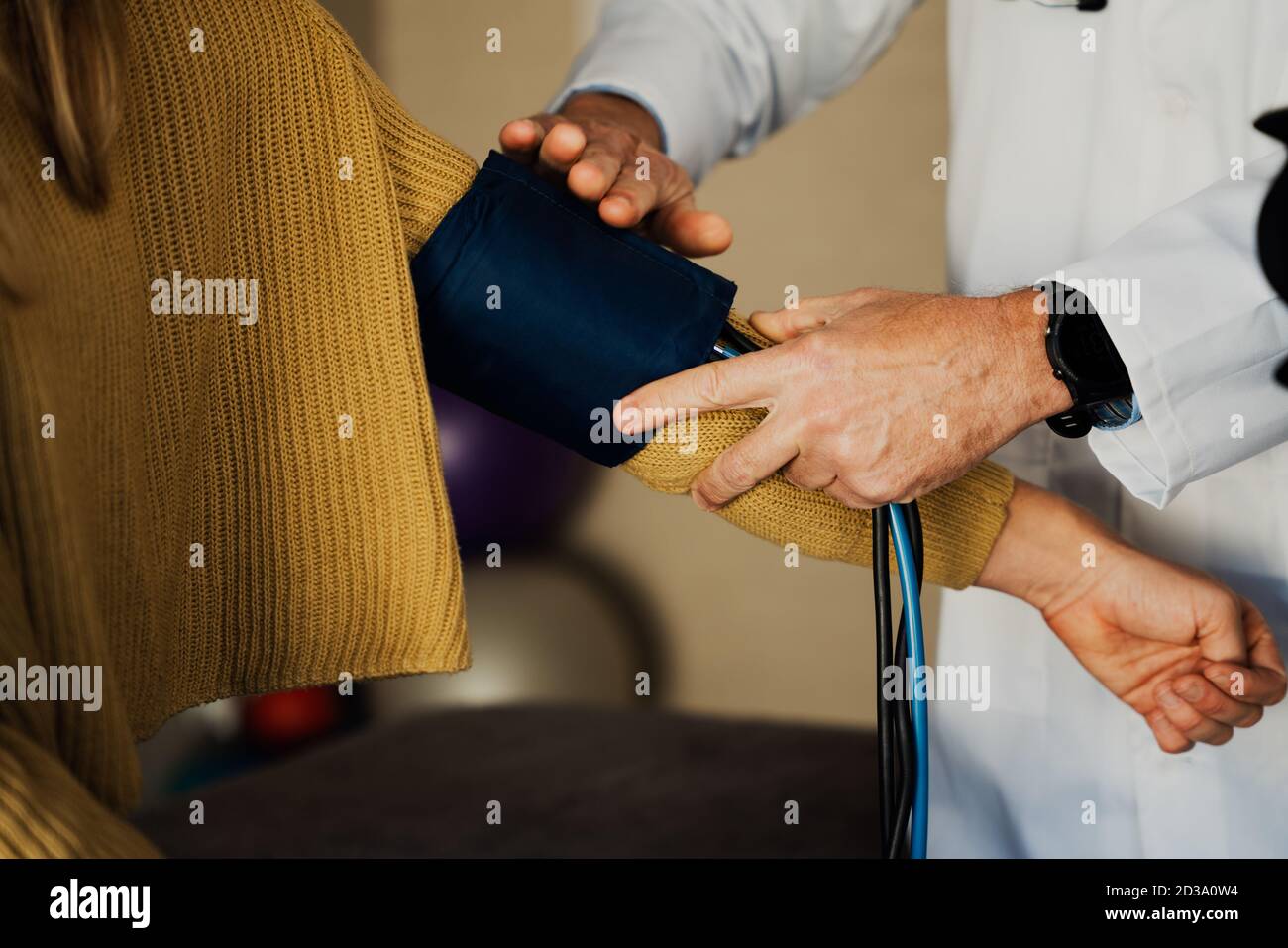 Male doctor removing blood pressure machine from female arm during checkup in doctors office. Stock Photo