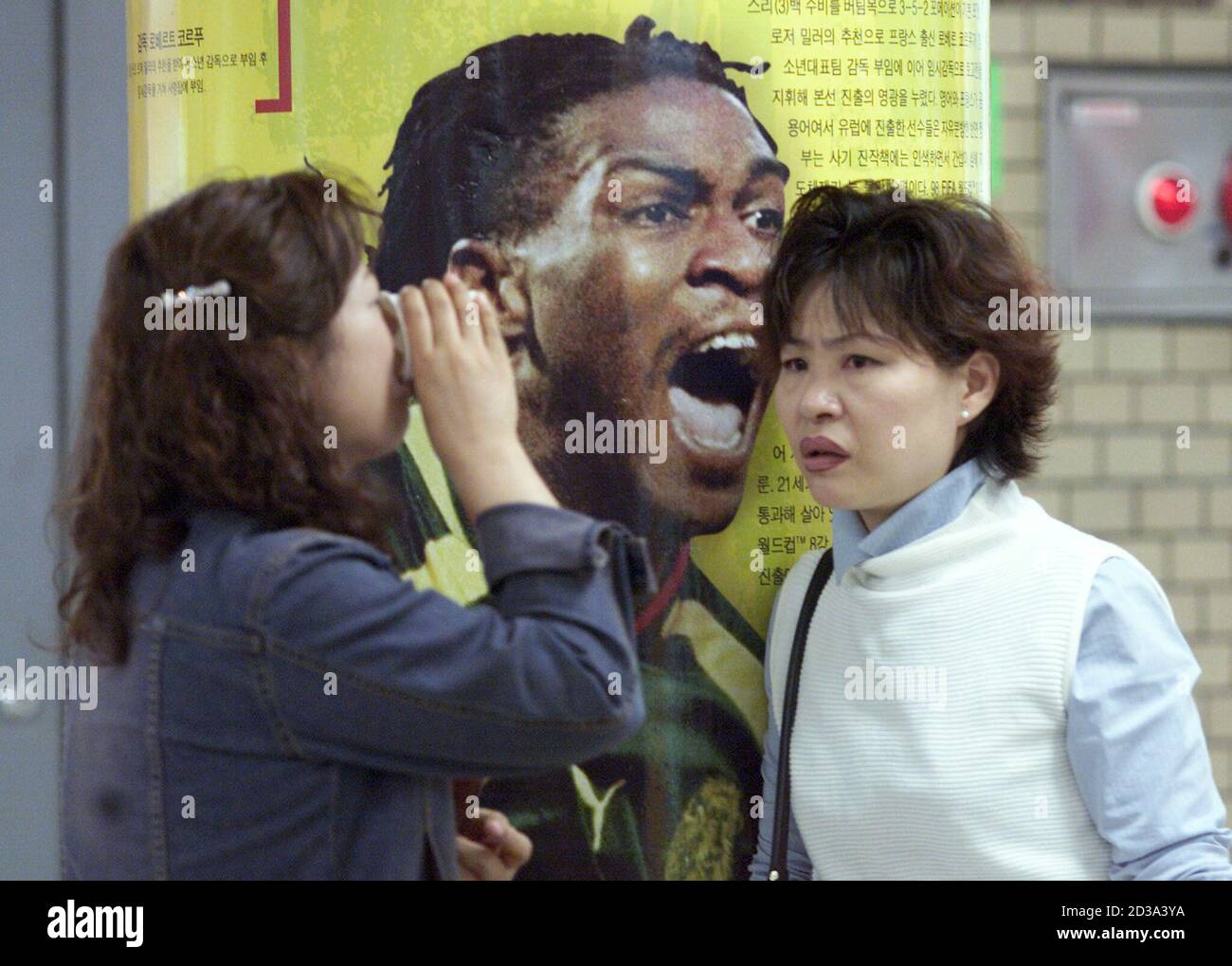 Korean women stand next to a subway station pillar bearing an action image of Cameroon's soccer star Rigobert Song in downtown Seoul May 6, 2002. As the 2002 soccer World Cup final draws nearer, with just 25 days until matches begin, host cities throughout Korea and co-host nation Japan are getting into the spirit of the tournament with giant posters and colourful decorations. REUTERS/Jason Reed  JIR/PB Stock Photo