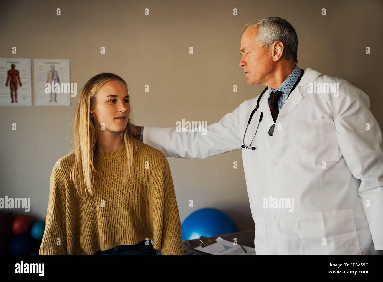 elderly male doctor assesses neck of young female patient Stock Photo